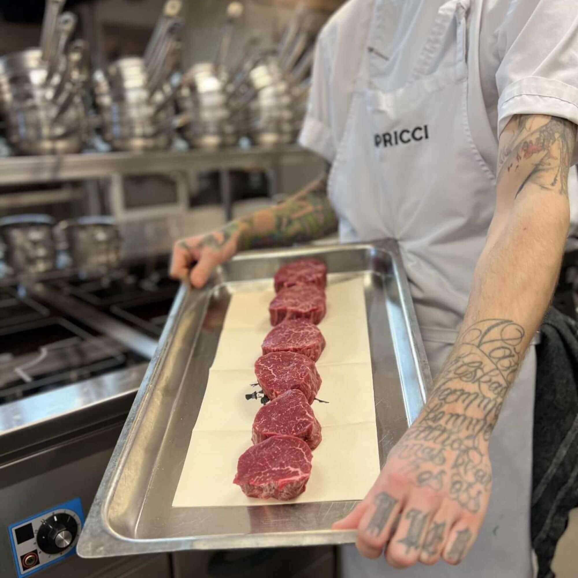 Een hele ossenhaas en enkele tournedos op een barbecue, met een kernthermometer in het dikste deel van het vlees en gloeiende kolen aan één zijde voor directe en indirecte hitte.
